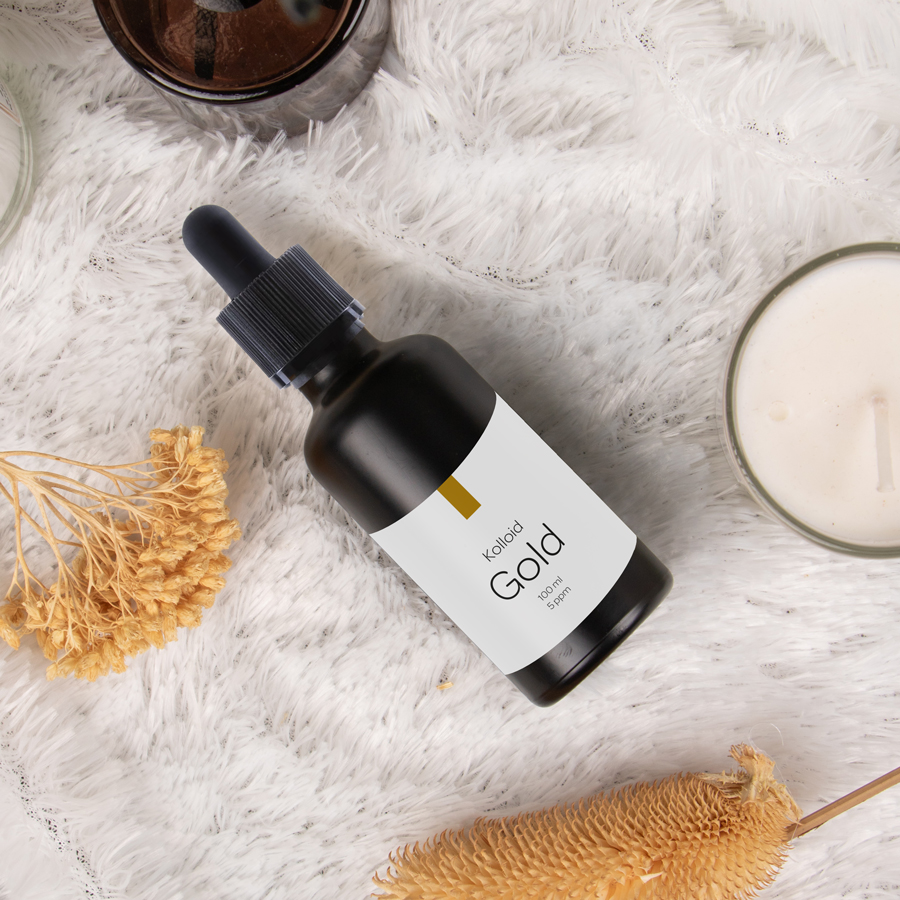 Fläschchen mit kolloidalem Gold auf weicher Unterlage, umgeben von Kerzen und Trockenblumen